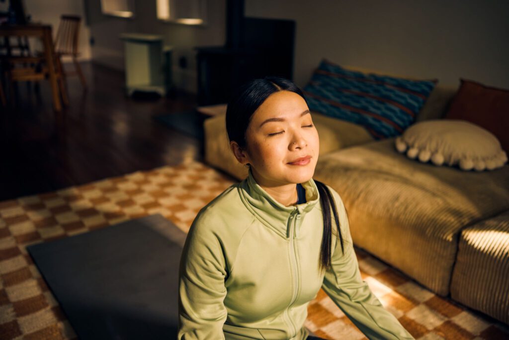 Woman meditating in sunlit living room.