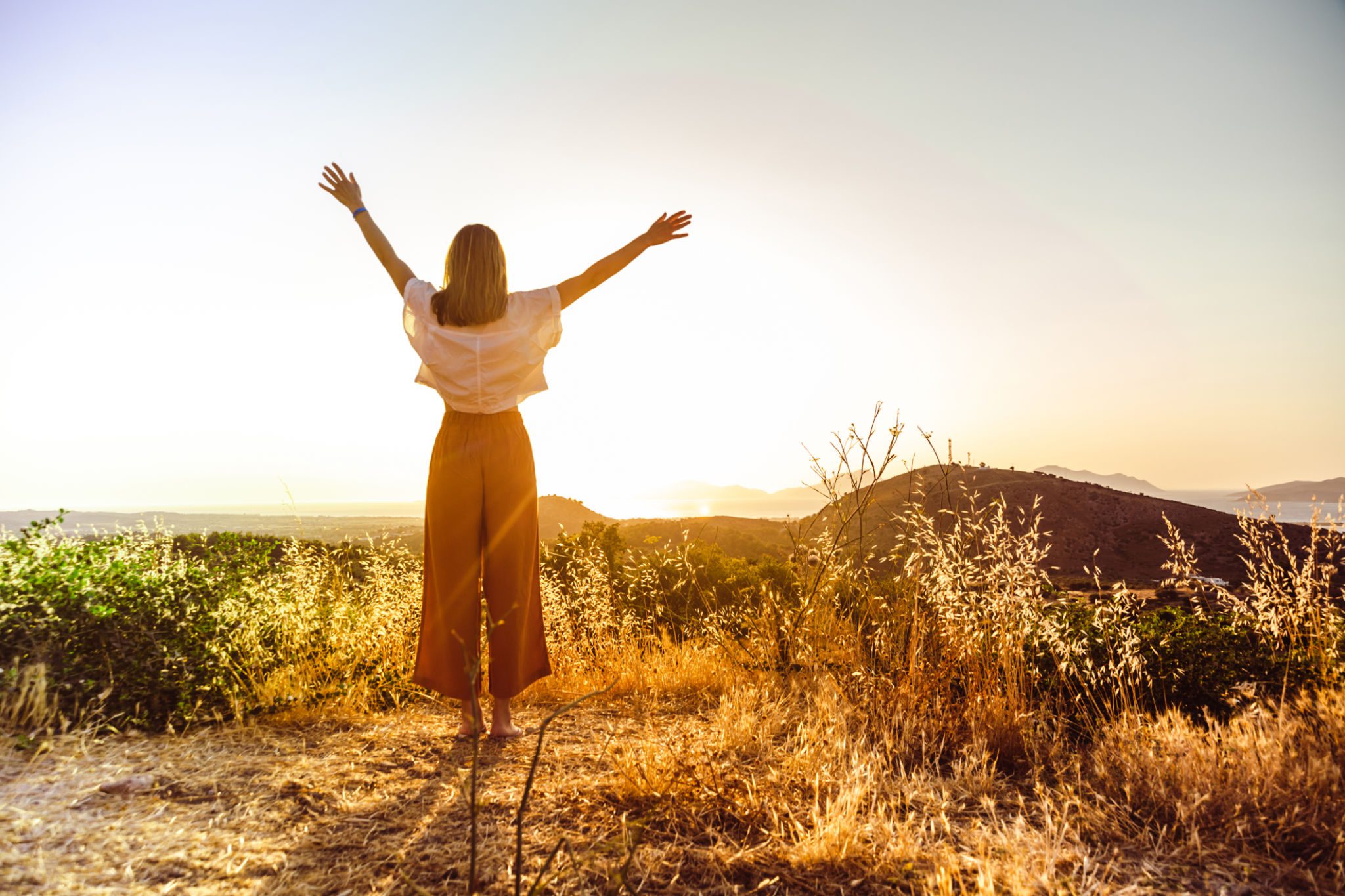 Person celebrating sunrise on a grassy hill.