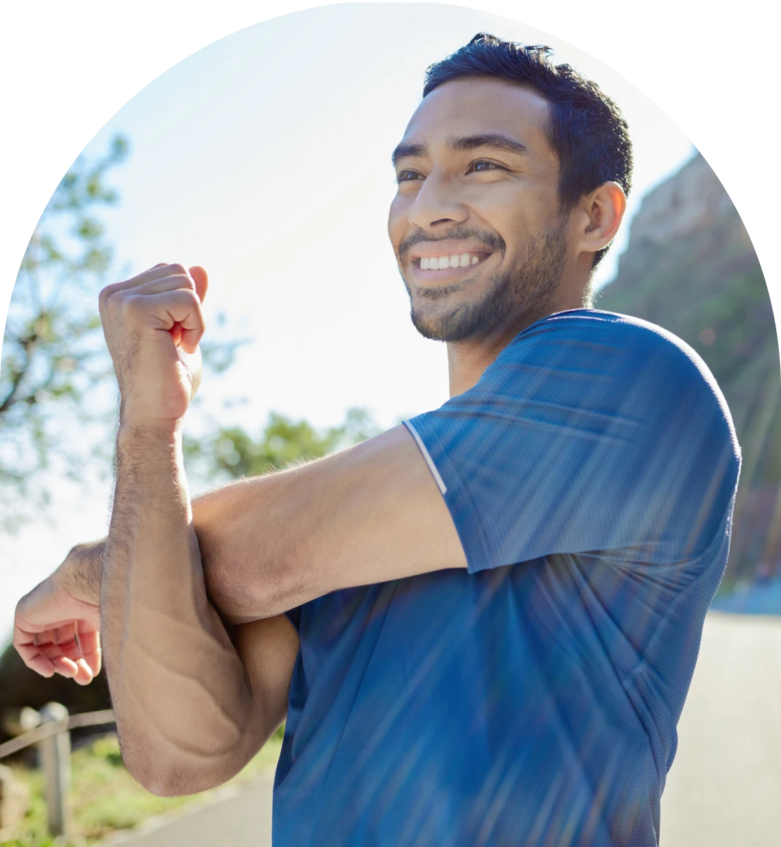 Man smiling while stretching outdoors in sunlight.